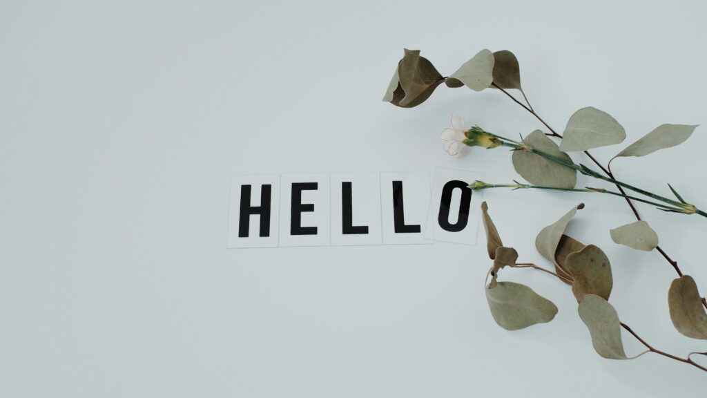 A minimalist flat lay featuring a 'HELLO' note with eucalyptus leaves on a white background.